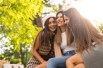 Women friends sitting hugging in a park in autumn at sunset, autumn lifestyle