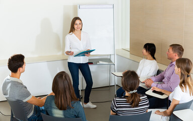 Wall Mural - Positive young female business coach communicating with adult auditorium during training in office