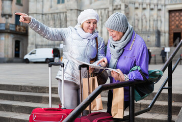 Senior woman with female friend traveling together looking for destination with city map.