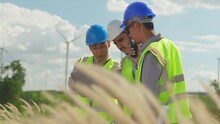 Three Asian Engineers Working In Wind Turbine Field. Men Worker Checking Plan For Construction On Wind Farms. Wind Turbine. Generate Electricity. Renewable Energy For Reduce Greenhouse Gas Emissions.