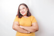 © Reezky - Portrait of a confident smiling big sized Asian woman wearing yellow shirt standing with arms folded and looking at the camera isolated over white background