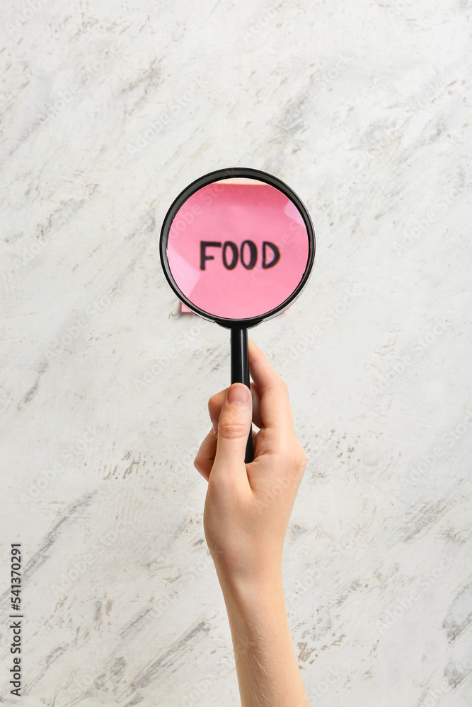 Female hand with magnifier and word FOOD on light background. Anorexia concept
