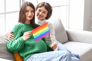 Wall Mural - Young pregnant woman with LGBT flag and her wife at home