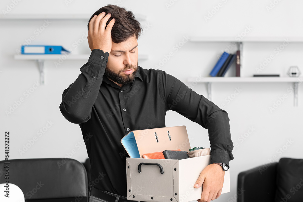 Sad fired young man holding box with personal stuff in office