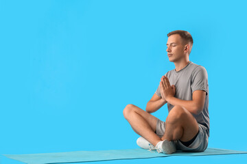 Poster - Sporty young man meditating on blue background