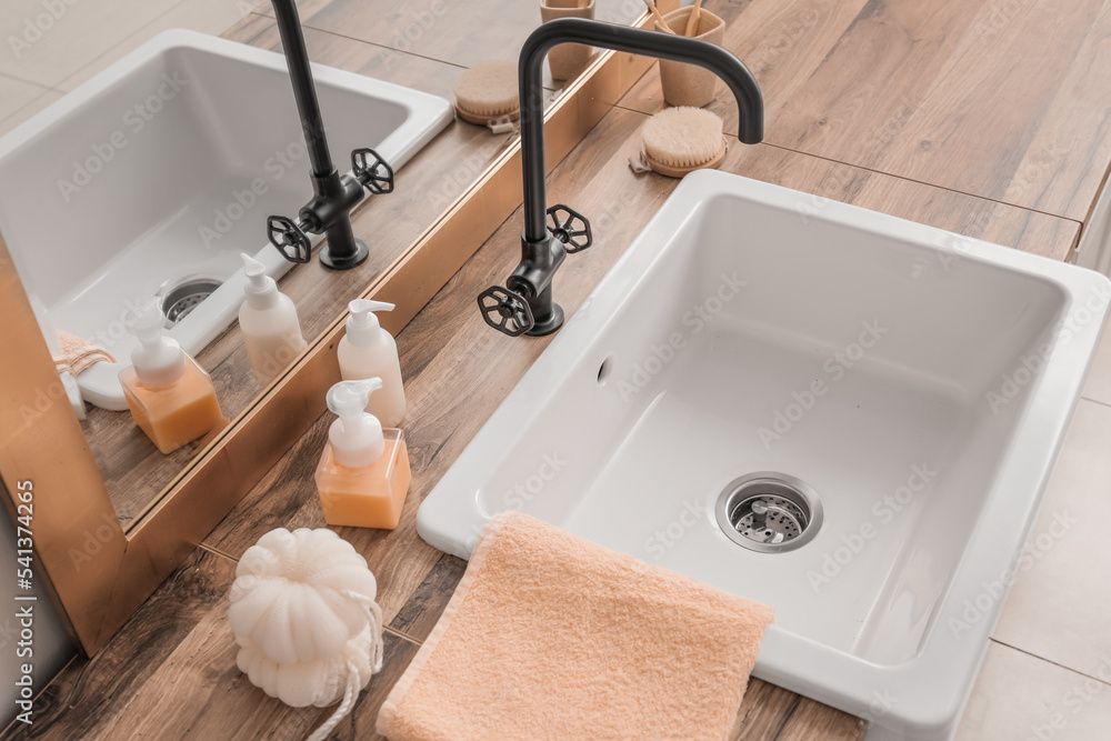 Bath accessories, sink and mirror on table near light wall