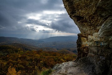 Poster - Closeup of a mounatian rock on a background of autumn coloful forests under the cloudy sky