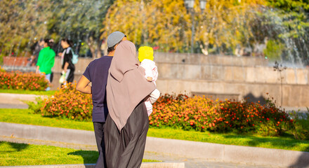 Wall Mural - Muslim family spend time together in the park. Girl in a hijab. Romantic Muslim couple in love with a baby in their arms.