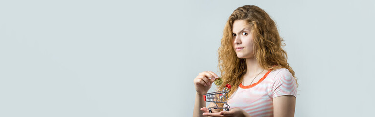 Young red-haired curly girl over white background holding piggy bank and rejoices gesturing. The concept of reliability of cash investments and insurance. Girl puts in the piggy bank physical Bitcoin