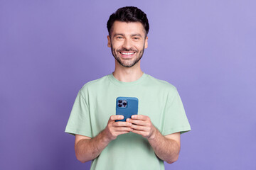 Poster - Photo portrait of attractive young man holding device toothy beaming smile dressed stylish gray clothes isolated on purple color background