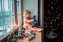 Cute Little Girl Is Dressing Up A Tiny Christmas Tree And Trying On New Year's Animal Masks. Image With Selective Focus And Toning. 