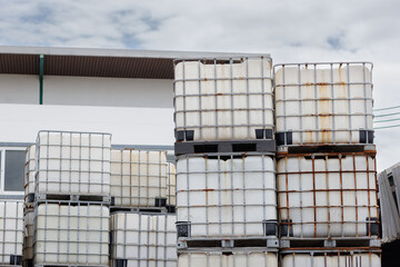 Wall Mural - stacked IBC containers with factory background. reuse white plastic chemical tanks in factory yard.