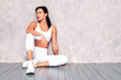 © halayalex - Fitness confident woman in white sports clothing. Sexy young beautiful model with perfect body. Female posing near grey wall in studio. Stretching out before training. Having relax, break