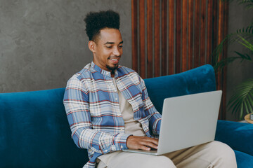 Sticker - Young happy IT man wear casual shirt sits on blue sofa couch hold use work on laptop pc computer stay at home hotel flat rest relax spend free spare time in living room indoors People lounge concept.