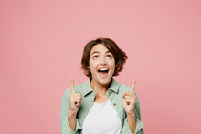 Young Surprised Shocked Cool Woman 20s Wear Green Shirt White T-shirt Point Index Finger Overhead On Workspace Area Mock Up Copy Space Isolated On Plain Pastel Light Pink Background Studio Portrait.