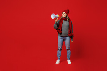 Full body young woman wear grey sweater scarf hat hold scream in megaphone healthcare information isolated on plain red background studio. Healthy lifestyle sick disease treatment cold season concept.