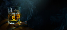 A Glass Of Whiskey With Ice On An Oak Barrel And A Smoking Cuban Cigar On A Dark Background. Men's Club Banner Idea. Copy Space For Text