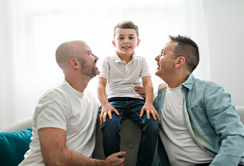 Wall Mural - Happy two man couple with adopted child sit on sofa at home