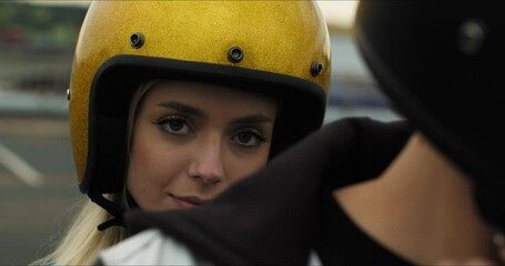 Wall Mural - Close-up portrait of a young attractive girl sitting on a motorcycle behind her boyfriend. Couple in love putting on helmets on a bike