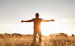 Having a positive mindset, wellbeing and hope concept. Happy young man standing in a nature sunrise field with arms outstretched.	