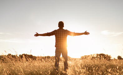 Having a positive mindset, wellbeing and hope concept. Happy young man standing in a nature sunrise field with arms outstretched.	