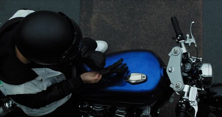 Wall Mural - Man motorcycle rider takes black leather glove and puts on hand sitting on blue classic motorbike. Top view