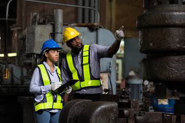 Wall Mural - Group of male and female engineer worker checking or maintaining heavy metal machine at the industry factory area. Team of technician wear safety uniform working and discussion in the factory