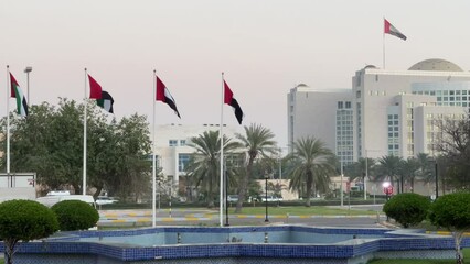 Wall Mural - United Arab Emirates flag waving around Abu Dhabi city landmarks - Aerial high view of the capital of UAE - corniche towers