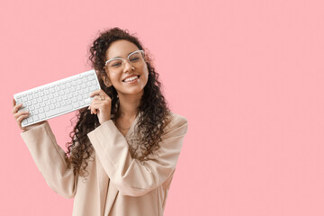Wall Mural - Young African-American woman with computer keyboard on pink background