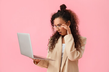 Shocked young African-American woman using laptop on pink background