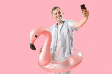 Canvas Print - Young man with inflatable ring and mobile phone taking selfie on pink background