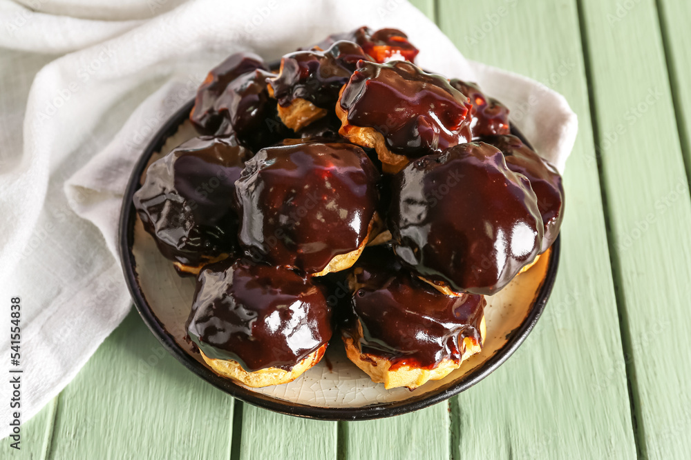 Plate with delicious eclairs on color wooden background