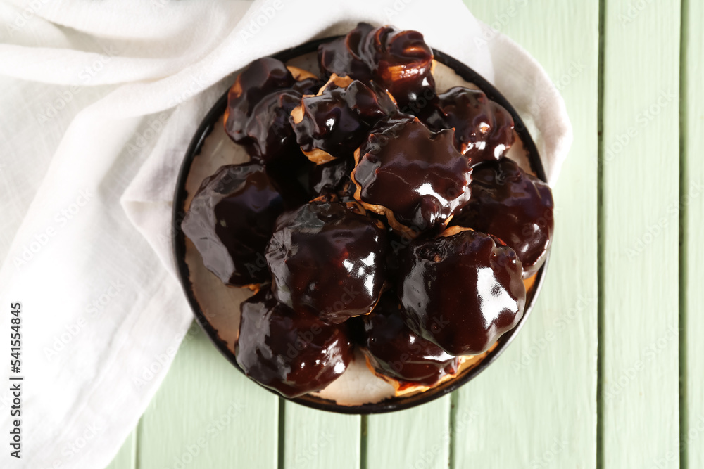 Plate with delicious eclairs on color wooden background