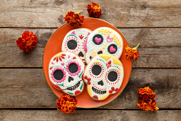 Plate with skull shaped cookies and flowers on wooden background. El Dia de Muertos