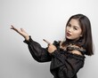 Filipina in a vampire costume pointing to the side with index finger and palm on white background