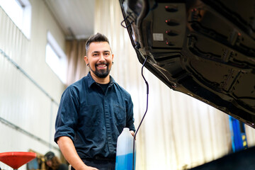 Wall Mural - Handsome mechanic job in uniform working on car holding Windshield Washer Fluid