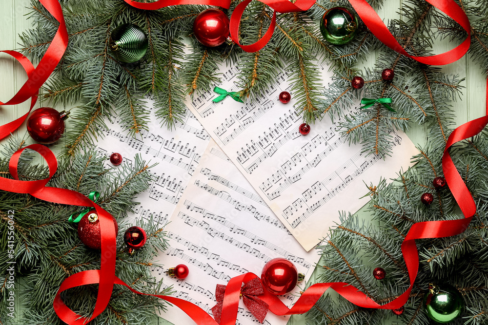 Note sheets with Christmas branches, balls and ribbon on green wooden background