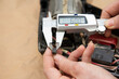 Manos con un calibrador digital, midiendo las escobillas de carbón de una herramienta eléctrica