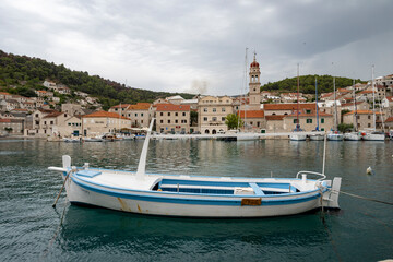 Sticker - Beautiful blue and white fishing boat in front of Pucisca church, Croatia with wildfire smoke visible in the distance