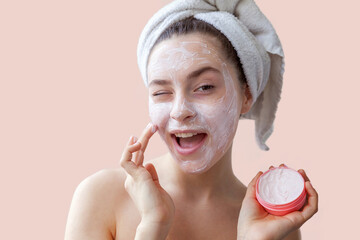 Wall Mural - Beauty portrait of young woman in towel on head applying white nourishing mask or creme on face isolated on pink background. Skincare cleansing eco organic cosmetic spa relax concept.