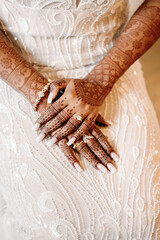 Wall Mural - Close-up hands of bride with henna drawings and silver engagement ring, holding hands on a wedding dress with beads
