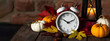Fall winter time change concept. Autumn composition with retro alarm clock, bright yellow and red leaves, pumpkin, walnut, candle lantern. Brick wall. Cozy home atmosphere. Close-up banner copy space