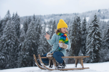 Wall Mural - Boy sledding, enjoying sleigh ride. Child sitting on the sleigh. Children play with snow.