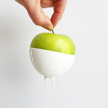 Close-Up Of A Hand Holding A Green Apple Dipped In Paint And Merging Into The Background