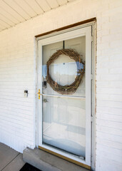 Wall Mural - Vertical Front exterior of a house with glass storm door over the white door with large leafless wreath