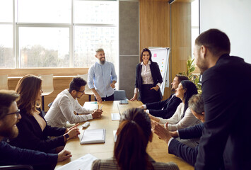 Wall Mural - Smiling diverse trainers or coaches make flipchart presentation for businesspeople at team training in office. Business speakers present project on whiteboard for employees in office on seminar.