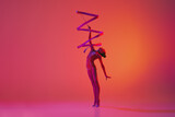 Young flexible teen girl rhythmic gymnast in motion, action isolated over pink background in neon light. Sport, beauty, competition, flexibility, active lifestyle