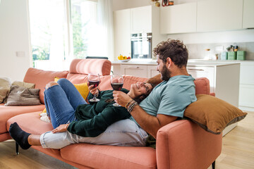 Heterosexual Romantic couple of young people relaxing carefree on the couch drinking wine - newlywed family having fun bonding on the sofa enjoying their new home - lifestyle concept