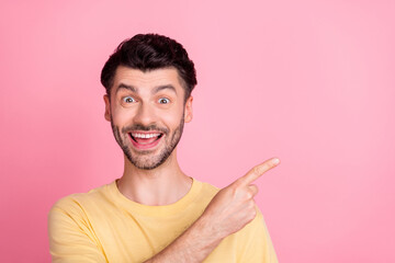 Sticker - Portrait of ecstatic positive crazy man with stylish haircut wear yellow t-shirt directing empty space isolated on pink color background