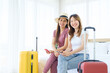 © artitwpd - Two happy Asian women looking at the camera while sitting together on the bed with their luggage. Planning on a holiday vacation trip. Image with copy space.